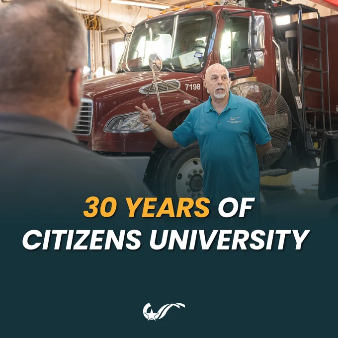 An individual in a blue Citizens University shirt speaks in front of a red truck with "7198" on it. Text on the image reads "30 Years of Citizens University." Another person is partially visible in the foreground.