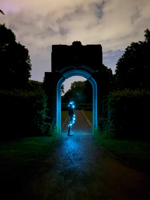 person with an led strip around their body inside an arc at night illuminating their surroundings 