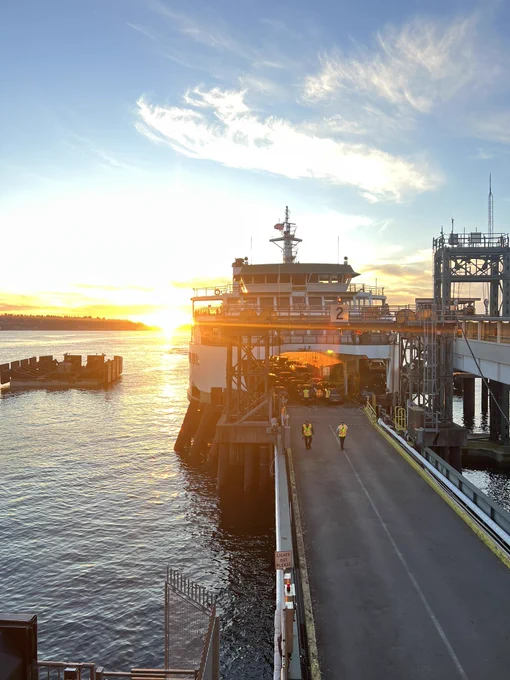 A docked ferry at sunrise with two people in safety vest walk towards the camera.