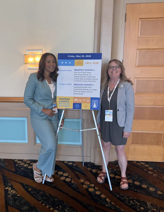 Tiara and Jen standing on either side of a colorful, blue, yellow, and white conference sign that says: "Friday, May 29, 2026" at the top. The session name in the middle: "BREAKOUT SESSION 5: Leading the Work: How Community Schools Can Align Efforts & Reduce Chronic Absenteeism" and the conference title in the bottom right corner, "Guiding Lights: Brighter Futures"