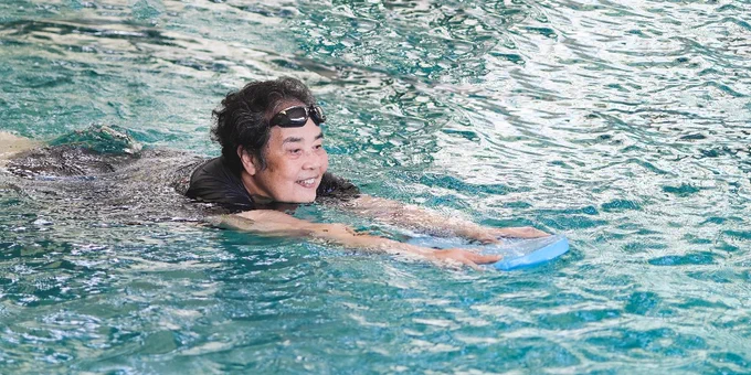 Person swimming in a pool using a blue kickboard for support and practicing swimming techniques.