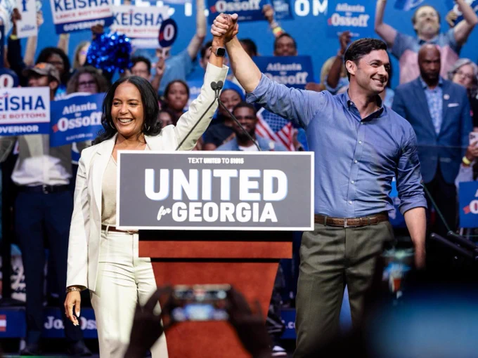 An image of Senator Jon Ossoff campaigning with Democratic nominee for Georgia governor Keisha Lance Bottoms. The two are holding hand each other's hand above their hands while smiling to a the crowd. The podium in front of them has a sign that reads, "United for Georgia." 