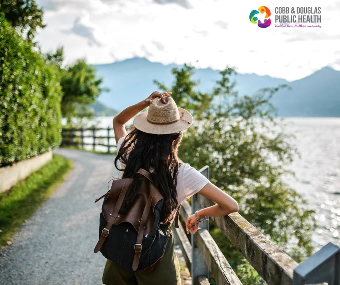 Woman with a backpack and hat enjoying a scenic lakeside walk on a sunny day.