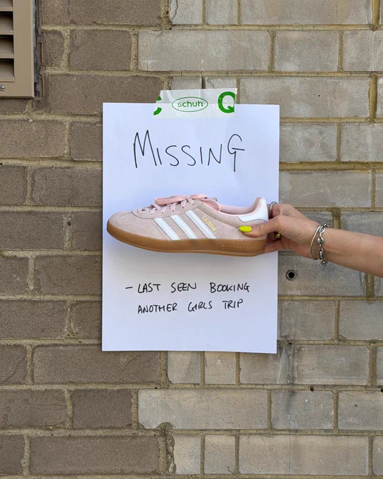 An image of a person's hand holding a pale pink adidas Gazelle Indoor trainer in front of a white piece of paper with text saying "Missing - last seen booking another girls trip".