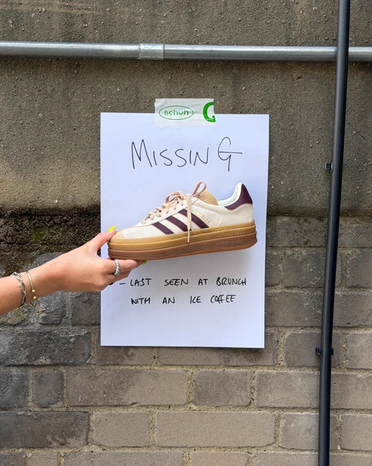 An image of a person's hand holding a beige adidas Gazelle Bold trainer in front of a white piece of paper with text saying "Missing - last seen at brunch with an ice coffee".