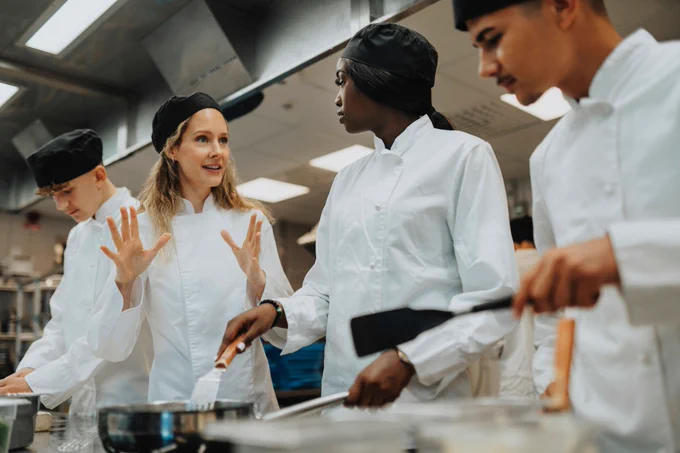 Group of chefs in white uniforms collaborating and discussing cooking techniques in a professional kitchen.