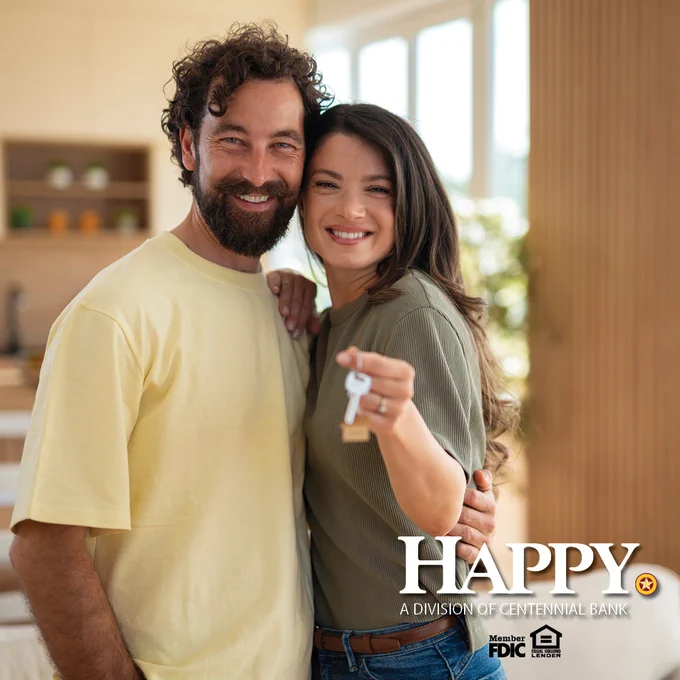 Couple standing in a bright home holding a key, symbolizing new homeownership and happiness.