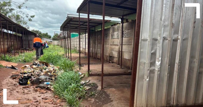 Photo taken in an informal settlement in Harare, showing people walking away from the camera alongside structures built from corrugated metal sheets and wood posts, with dumped waste on the path. Photo credit: Kudzai Chatiza