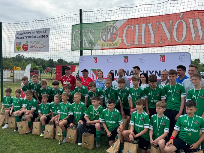 Zdjęcie grupowe, szeroki kadr. Uczestnicy spotkania pozują do wspólnego zdjęcia na boisku do piłki nożnej. W pierwszych dwóch rzędach stoją zawodnicy nagrodzeni podczas wydarzenia. Na zdjęciu widoczna między innymi Sekretarz Stanu Adriana Porowska.
