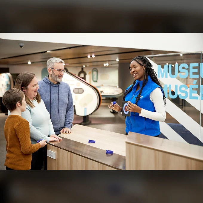 Au comptoir d’accueil, une famille s’adresse à une guide du Musée.