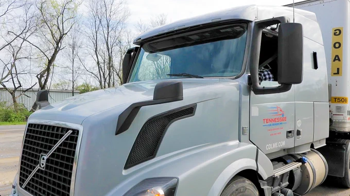 White Volvo semi-truck parked outdoors with Tennessee state decal on the door and a trailer attached.