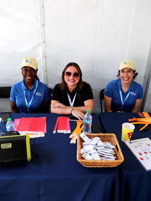 Three volunteers are seated behind a table at a booth