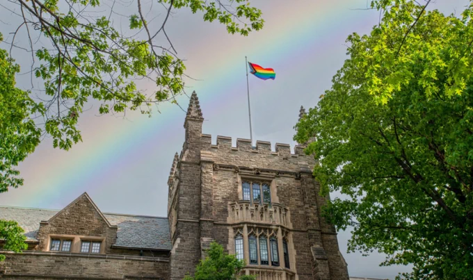 A Pride flag flying over McMaster's University Hall. There is a rainbow effect added to the sky the flag is set against. 