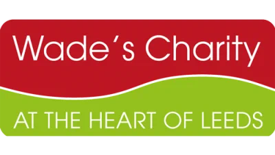 Image is a logo of Wade's Charity featuring a red upper section with white text and a green lower section stating 'At the Heart of Leeds'.