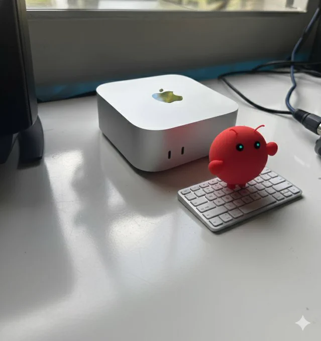 Small red robot character typing on a compact wireless keyboard next to a silver Apple Mac Mini for automation.