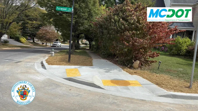 Newly constructed sidewalk corner with tactile paving at Foxwood Lane in Montgomery County, Maryland, featuring MCDOT signage.