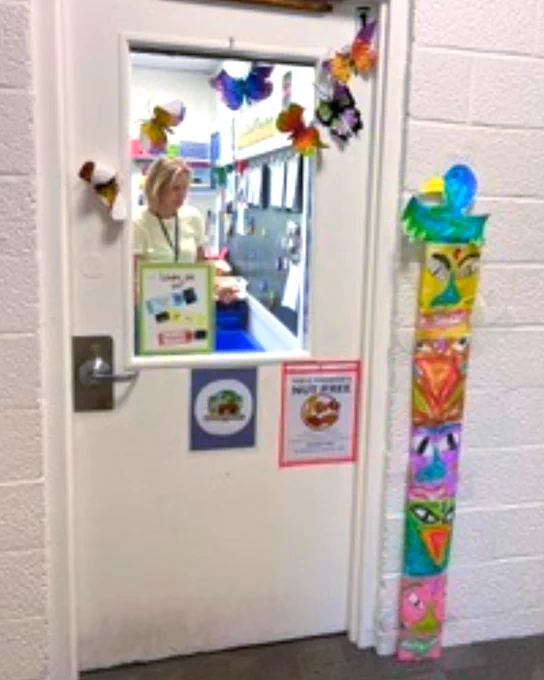 Classroom door decorated with colorful butterflies around the window and student artwork displayed on the wall beside it.
