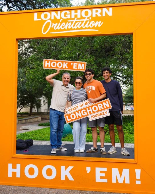 Family stands together holding signs celebrating UT Austin Orientation. 
