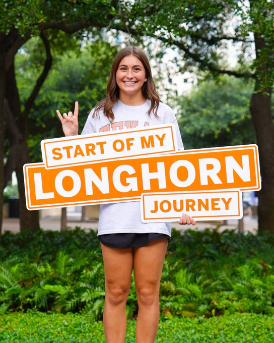 Person standing on the UT campus holding a sign that says \"Start of my Longhorn journey\".