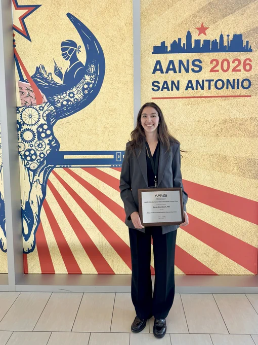 Dr. Sarah Sternbach poses with her plaque in front of signage for the AANS 2026 Annual Meeting in San Antonio