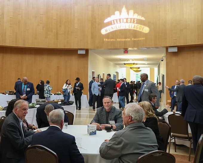 Attendees networking and conversing at a professional event hosted by the Illinois Municipal League in a spacious hall with wood-paneled walls.