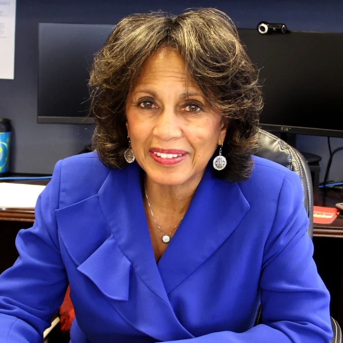 Smiling person with shoulder length dark hair wearing a ruffly blue top.