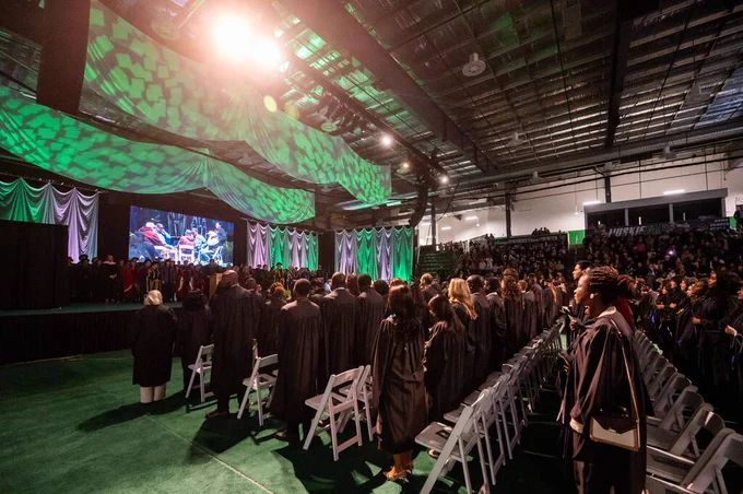 A group of graduates in caps and gowns walk in a procession during a graduation ceremony