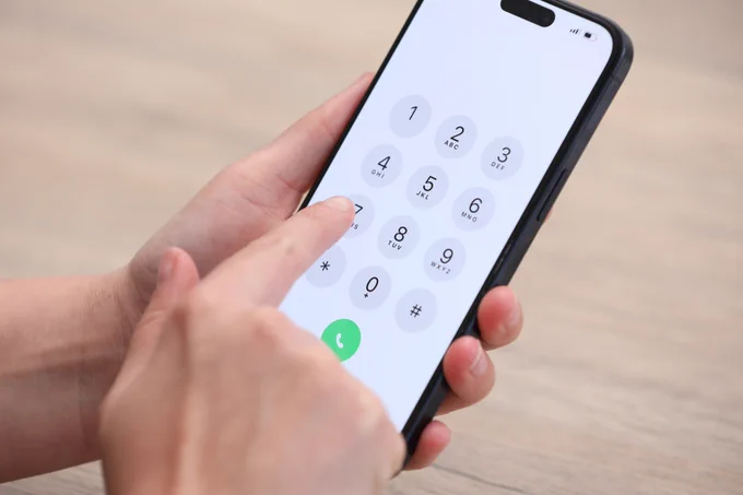Close up of person holding an iPhone in their hands, ready to type a phone number, with keypad visible on screen.