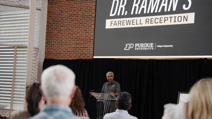 Dean Arvind Raman speaks at a Purdue podium at his farewell reception, with a large "Dr. Raman's Farewell Reception" screen behind him. 