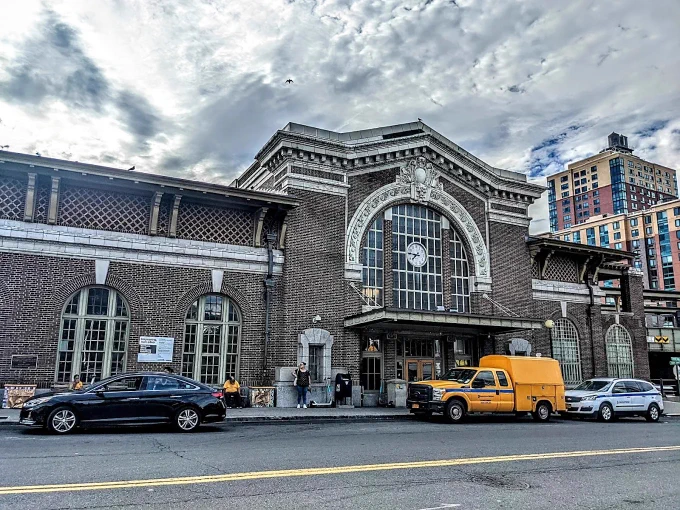 The Yonkers station facade on a cloudy day, with cars and trucks parked in front of it.