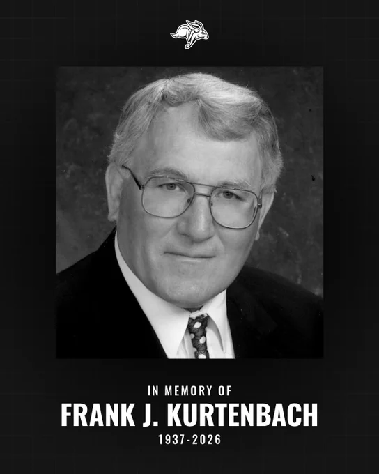 Black‑and‑white memorial portrait of an older man wearing glasses, a suit jacket, white shirt, and patterned tie, shown against a dark background. A small rabbit‑head logo appears above the image. Text below reads: “In Memory of Frank J. Kurtenbach, 1937–2026.”