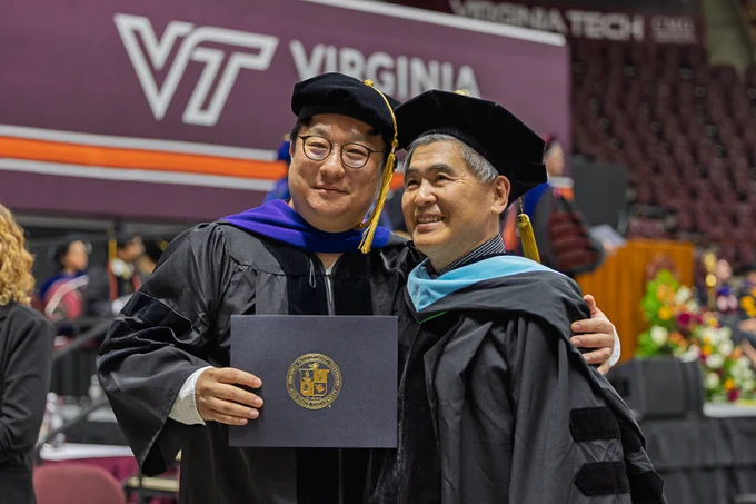 Graduate holding degree folder and posing with a faculty member for a picture
