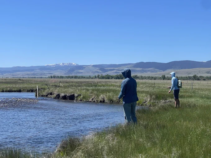 Two anglers on the banks on a Montana river with snow-capped mountains in the background.