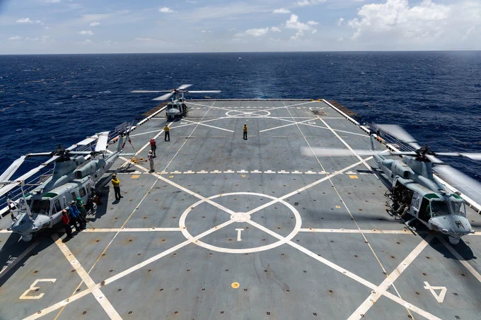 Marine helicopters and flight deck crews conduct coordinated aviation operations aboard a ship at sea.