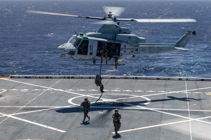 Marines fast rope from a helicopter onto a ship flight deck during maritime assault training.