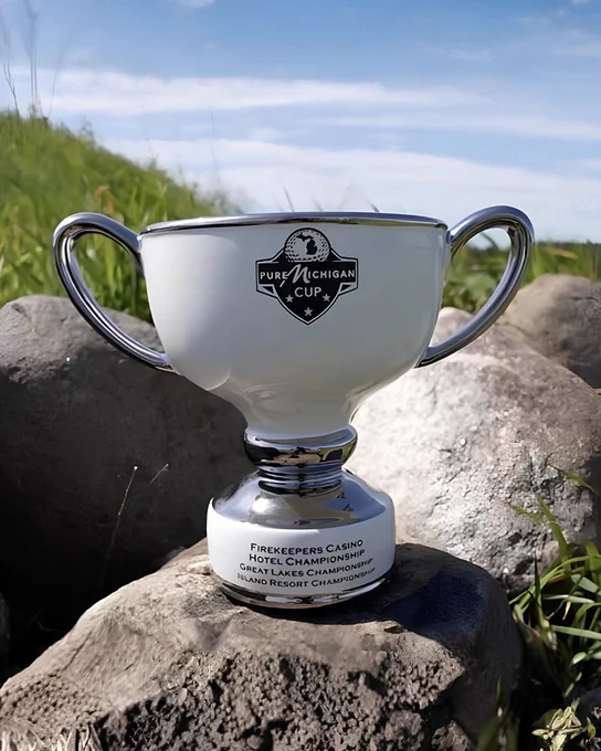 Pure Michigan Cup trophy displayed on a rock outdoors with the shoreline and water visible in the background.
