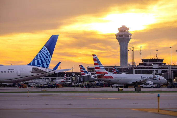 Sunset view at an O'Hare International Airport with United Airlines and American Airlines planes on the tarmac. The main airport control tower is visible in the background.