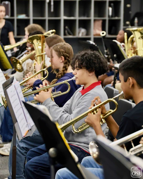 A group of students playing brass instruments, including trumpets and trombones, as part of a music class.