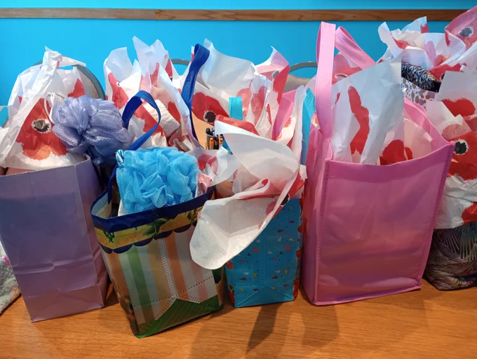 Colorful gift bags filled with floral-patterned tissue paper arranged on a wooden surface against a blue wall.