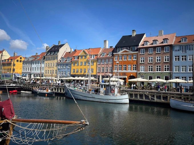 Colorful buildings and docked boats along a bustling waterfront quay under a clear blue sky.