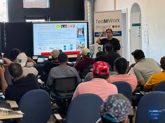 Participants sit in a classroom-style setup at Collège Boréal while a facilitator leads a presentation on eye health and safety, pointing to a slide in Spanish about preventing eye damage; a TeaMWork Project banner stands beside the screen.
