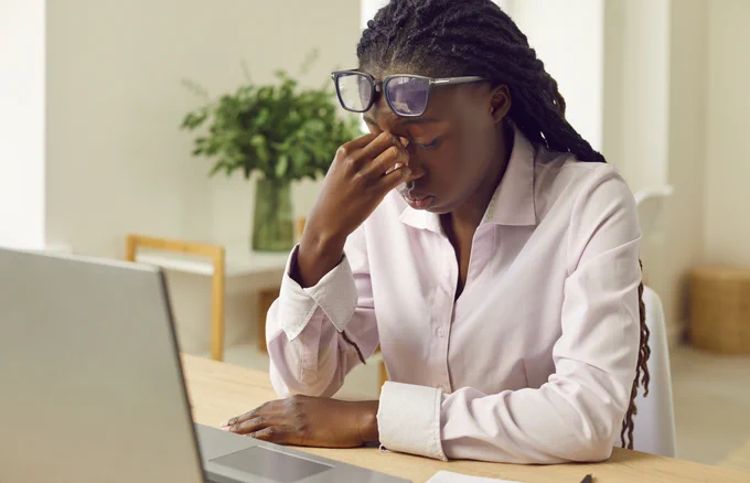Woman using a laptop, appearing exhausted in a clean, organized workspace.