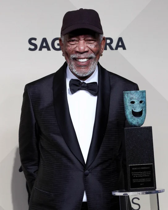 Morgan Freeman smiling with his SAG Life Achievement Award statuette on a pedestal in front of him. 