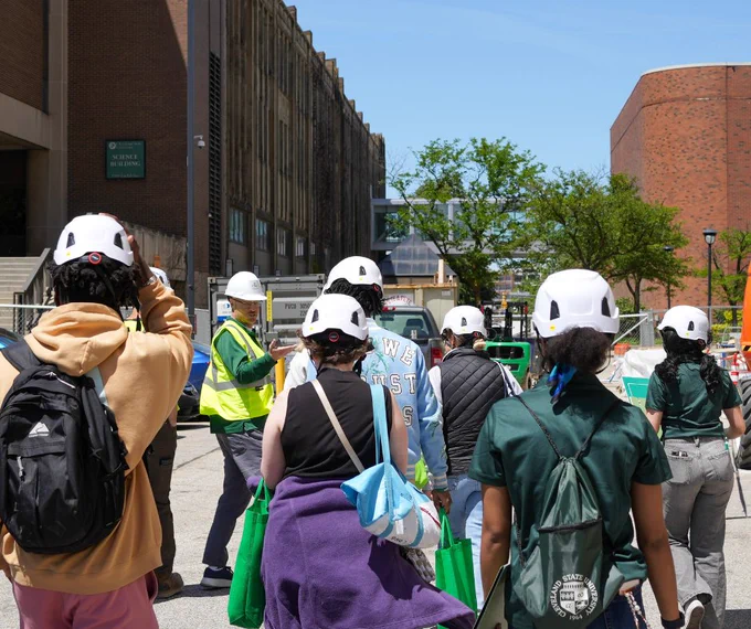 A group of prospective students wearing hard hats walking into Fenn Tower for a tour. 