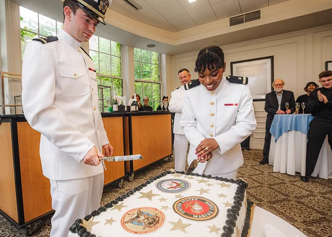 Two Columbia University students (Dana Clarke and Paul Randall) dressed in white naval uniforms cut a ceremonial cake with knives at their NROTC commissioning ceremony at Columbia University Faculty House.