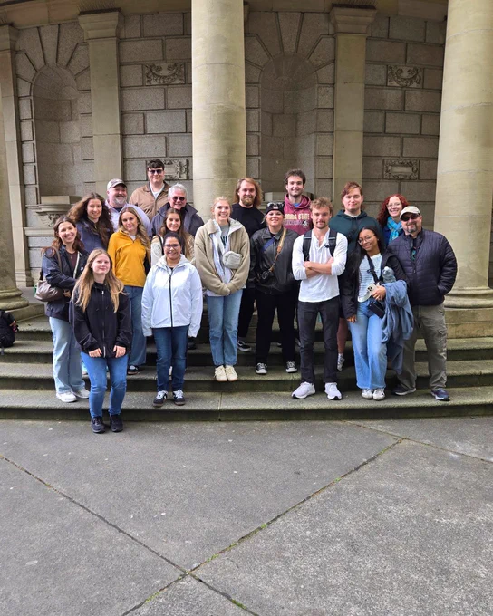Group of people posing on stone steps in front of a historic building with large columns and detailed stonework.