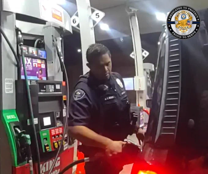 Police officer refueling a vehicle at a gas station pump during nighttime.