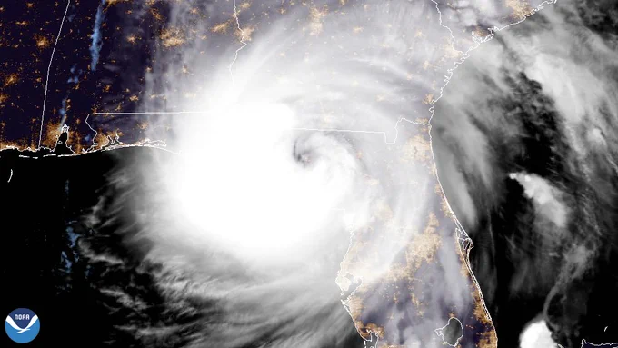 NOAA GOES-East satellite image showing Hurricane Helene making landfall along Florida’s Big Bend region at night on September 26, 2024. The large Category 4 hurricane fills much of the eastern Gulf of Mexico, with a defined eye approaching the Florida coast and dense spiral bands covering Florida and parts of the southeastern United States. City lights are visible beneath the storm clouds. NOAA logo appears in the lower left corner.
