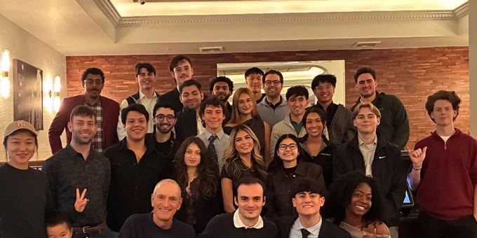 Large group of people posing together in a warmly lit room with brick walls and decorative ceiling details.