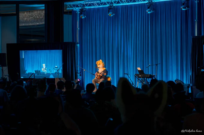 A fursuiter musician on a blue-lit stage at Anthrocon Tonight 2025.